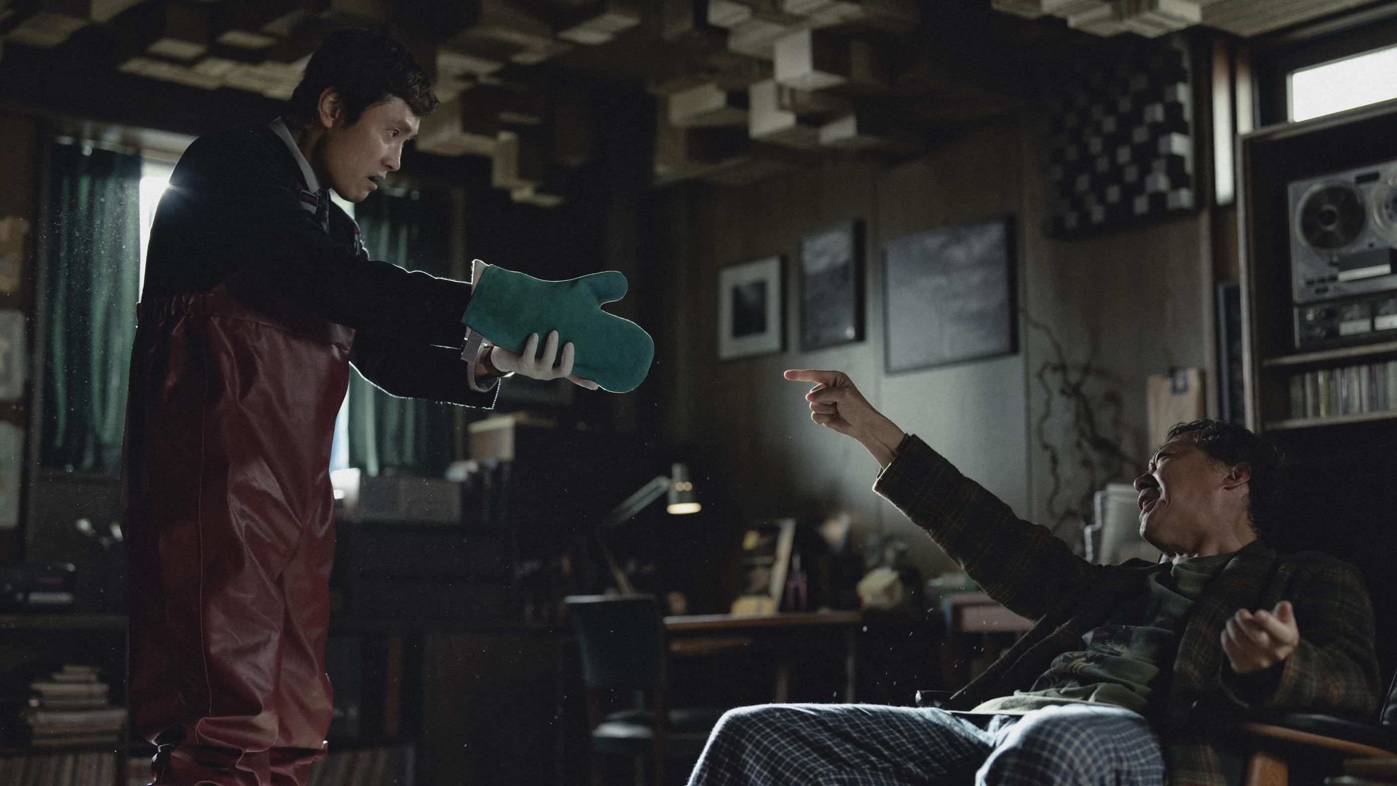 still from No Other Choice - a standoff between a man wearing a kitchen mitt and a guy making finger guns